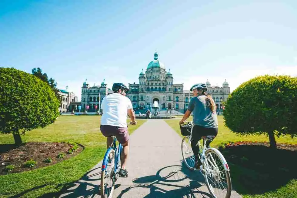 Two people riding bicycles in front of the british columbia parliament building.