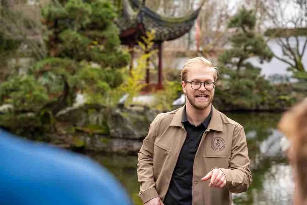 A man in glasses is standing in front of a pond.