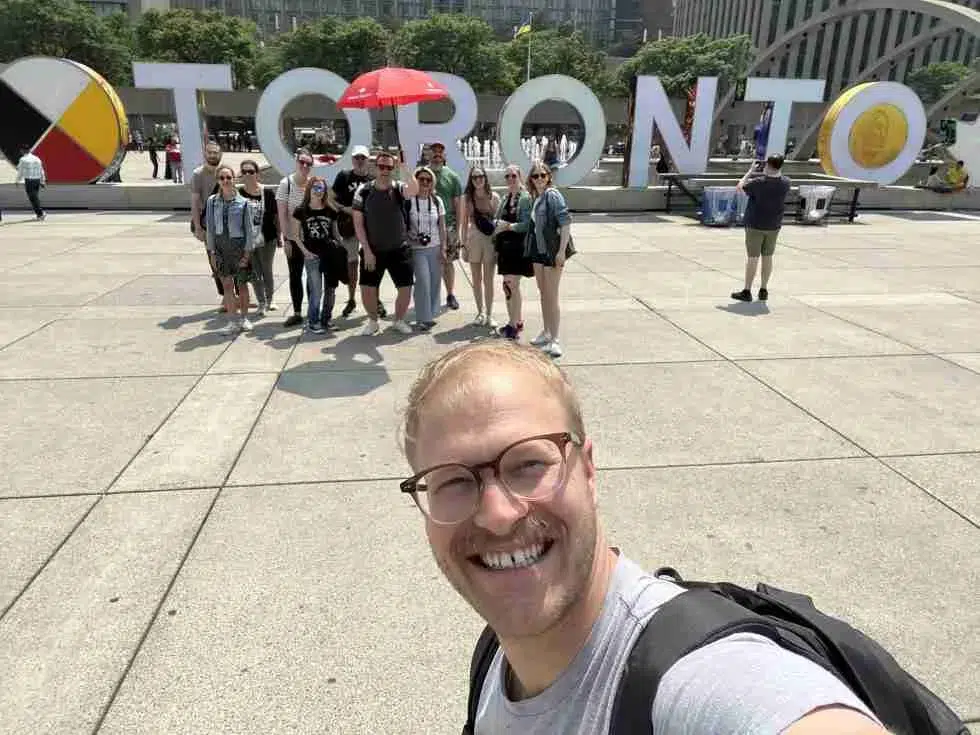 A man is taking a selfie in front of the toronto sign.