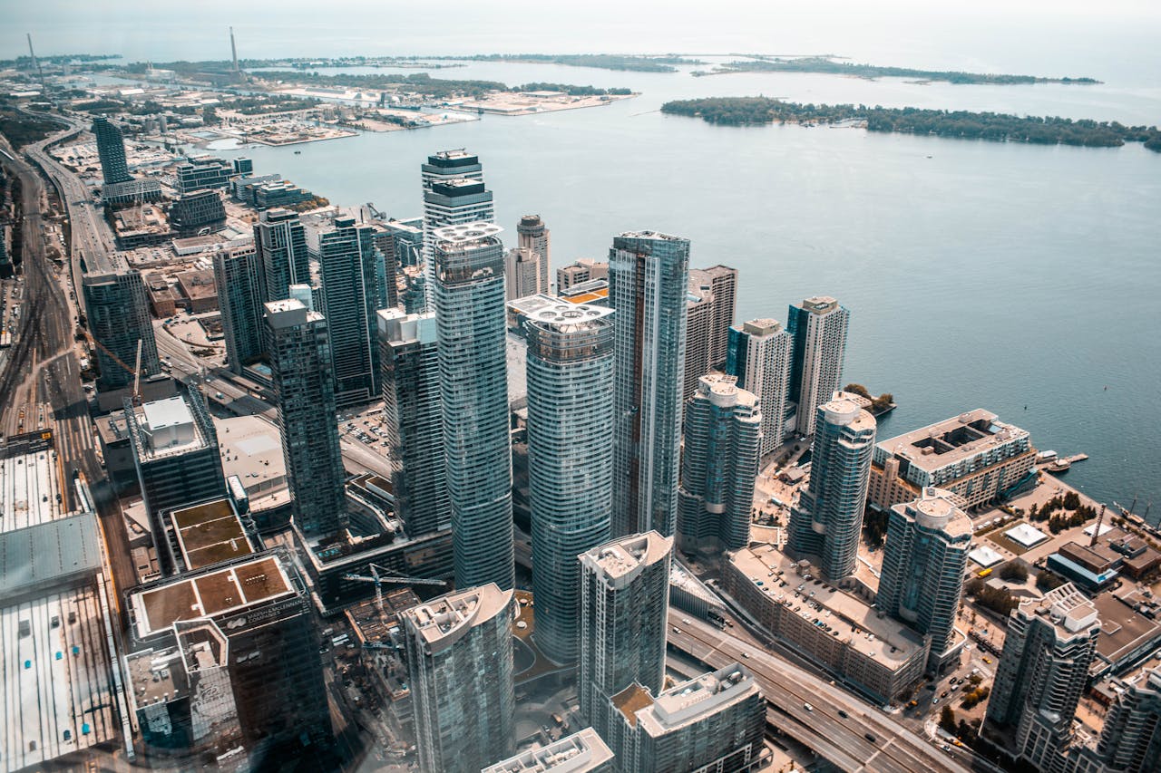 Aerial view of a cityscape featuring numerous tall skyscrapers and a large body of water in the background, showing urban development and waterfront areas.