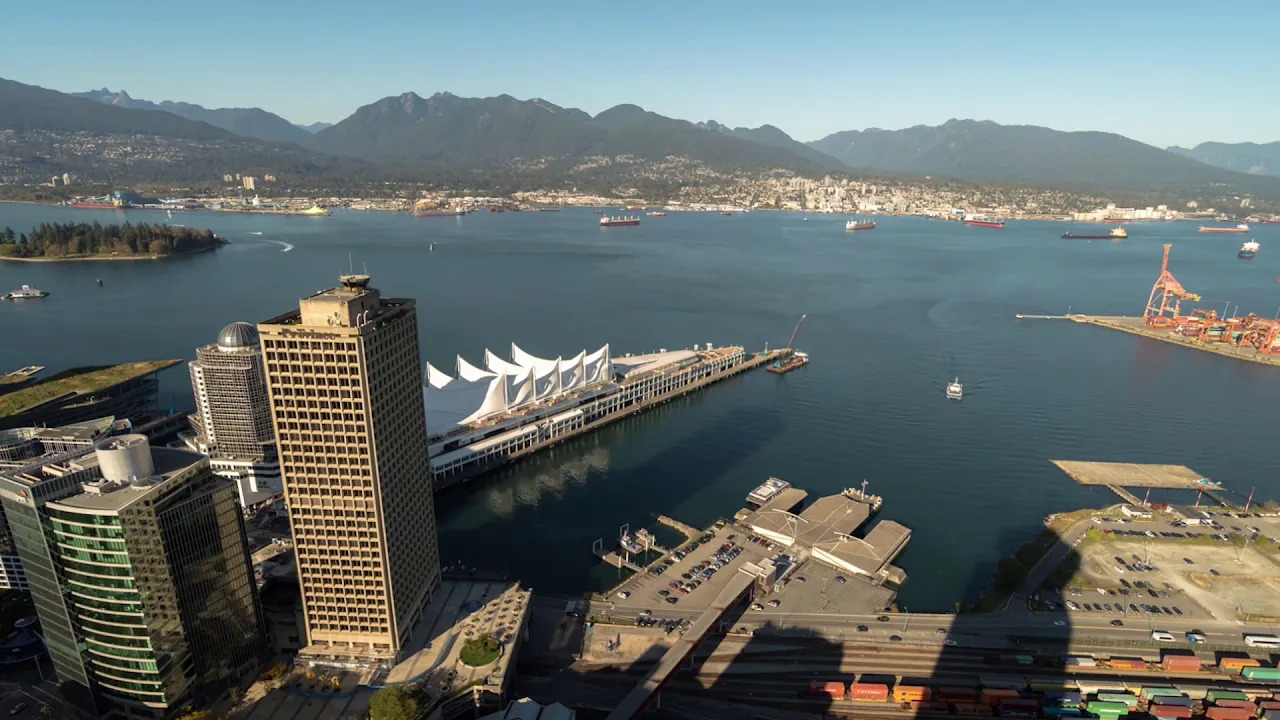 Aerial view of Vancouver Harbour with the Canada Place convention center, mountains in the background, and water vessels in the bay.