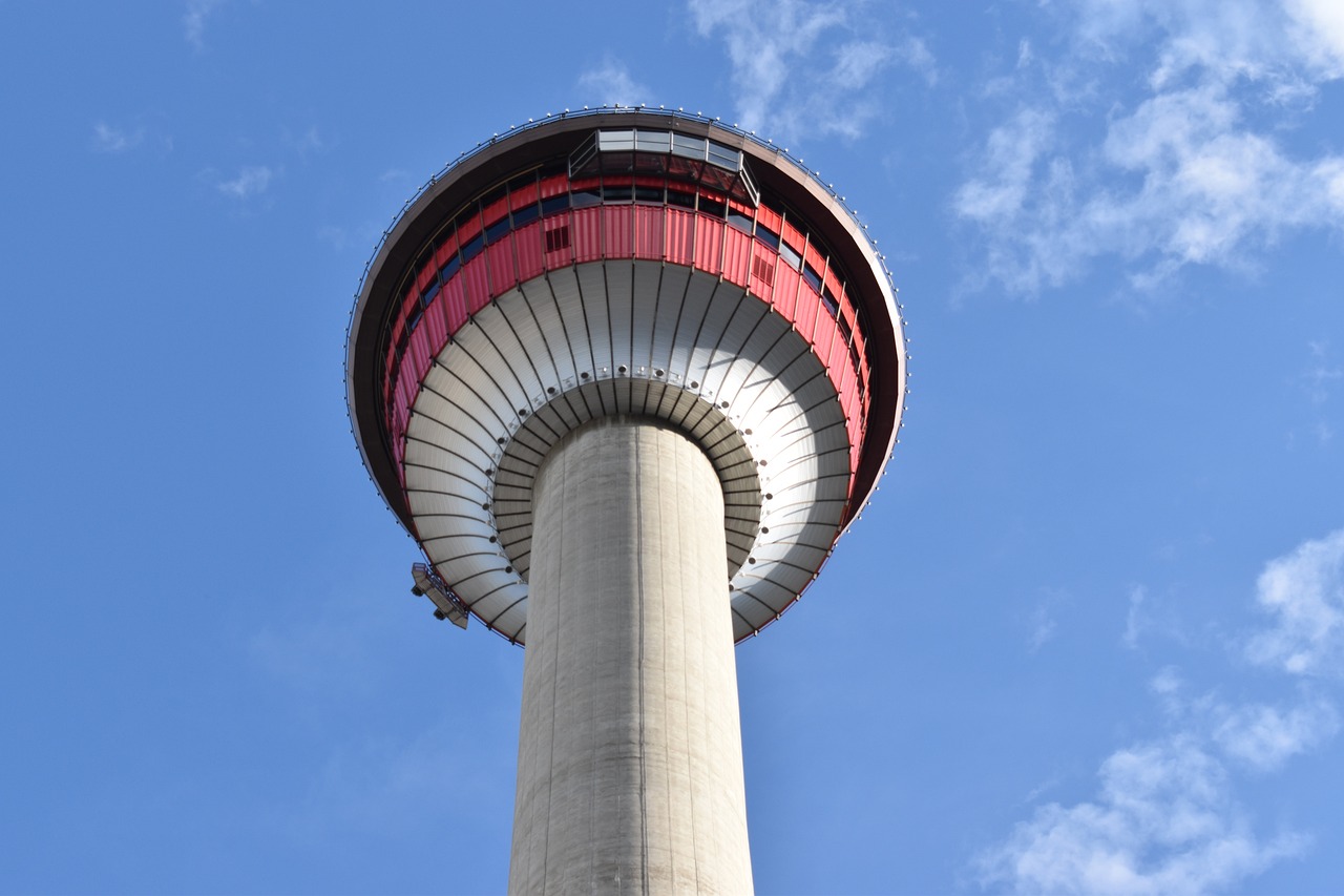 Close-up view of a tall observation tower with a circular, red and white observation deck against a blue, partly cloudy sky.