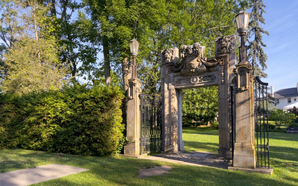 stone archway with ornate carvings and lanterns on each side, standing in a grassy park area with trees and bushes—one of the hidden gems toronto has to offer.
